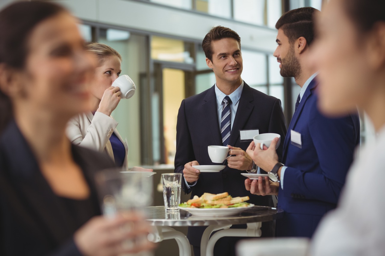 The image is centered on a young gentleman in a suit and tie with a cup of coffee in his hand. On his left hand side there's a woman sipping coffee, with another women who's blurred out covering her. On his right hand side is a gentleman in a dark blue suit sipping coffee. The webinar is a series that the Georgia Chamber is hosting where they will review the Chamber's mission, goals, and services to the business community.  image